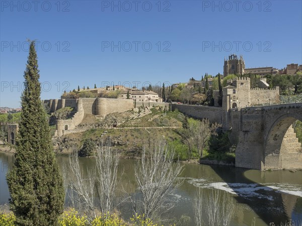 View of a fortress and historic walls over a river with cypress trees and green vegetation under a