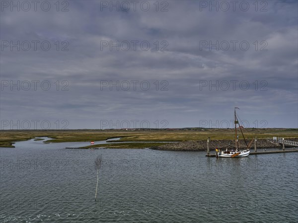Sailboat at a jetty surrounded by a watery landscape under a cloudy sky, small jetty with a