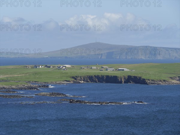 Peaceful coastal landscape with green hills and houses by the blue sea, green meadows by a deep