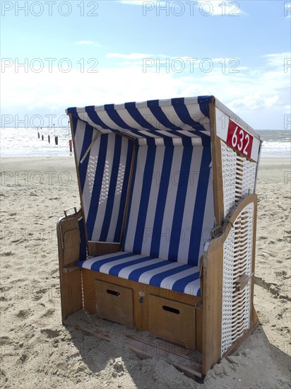 A single blue and white beach chair on the beach with the sea in the background and a cloudy sky,