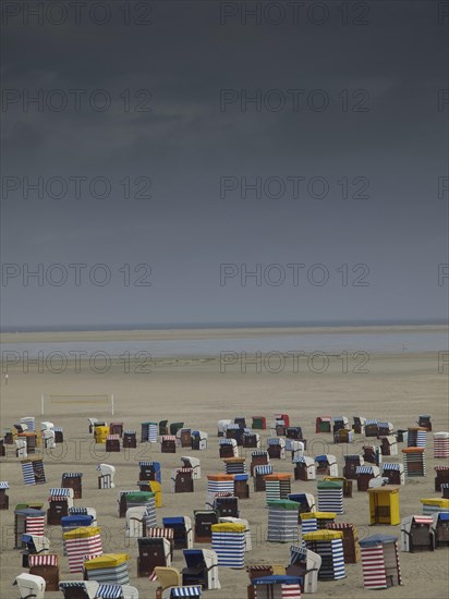 Dramatic sky over numerous colourful beach chairs on empty, wide beach with sea view, beach chairs