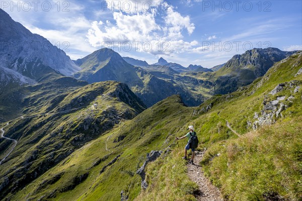 Mountaineer on a hiking trail on a grassy mountain ridge, idyllic mountain landscape with green