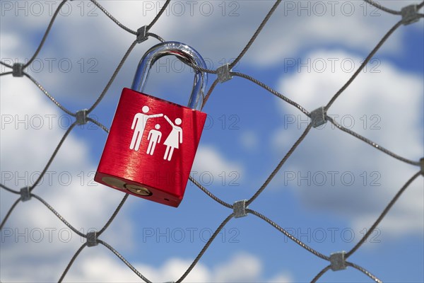 A single red love lock symbolising a family with a child hangs on a bridge railing over the Danube,