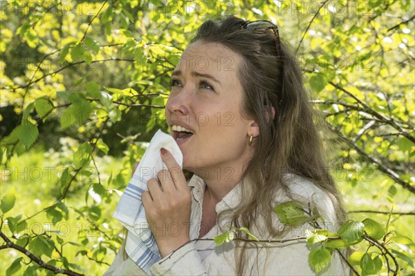 Young Caucasian woman, 35 years old, with allergy stands by flowering birch (Betula) in Ystad,