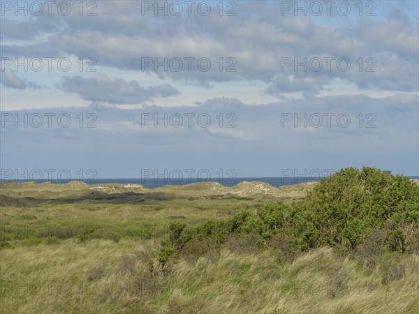 Vast landscape with hills and a view of the sea under a cloudy sky, dune and hiking trails on the