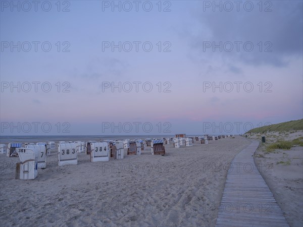 A long beach with white and striped beach chairs in the soft evening light and a wide wooden