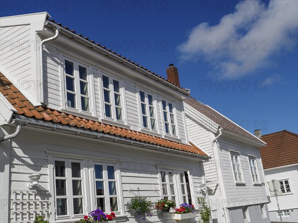 White house with red tiled roof, blooming flowers in the foreground under blue sky, white wooden