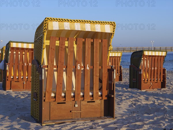 Close-up of a beach chair on the beach with other baskets and a pier in the background, beach