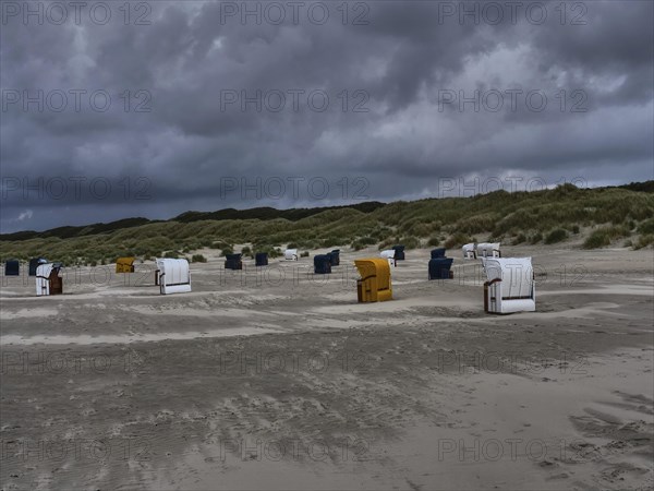 Beach chairs standing on a grey beach under a threatening cloudy sky, dunes in the background,