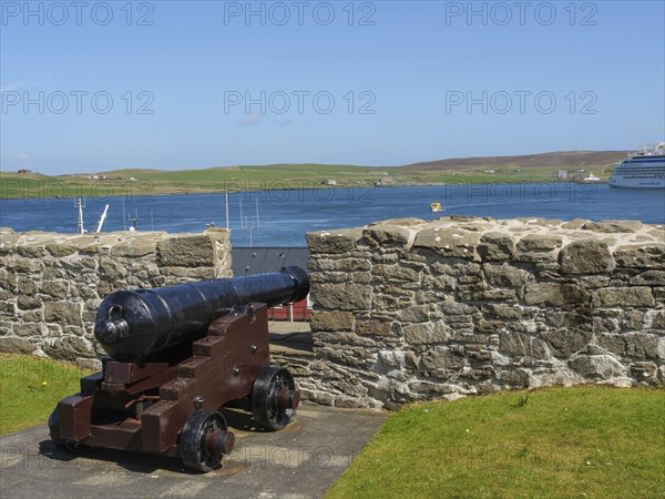 Historic cannon in front of a stone wall with a view of the sea, a ship and green hills, old