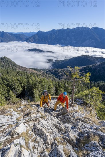 Two friends, mountaineers climbing the via ferrata to the rocky summit of the Ettaler Manndl, view