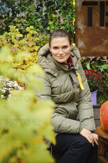 Cute woman in down jacket surrounded by flowers and leaves