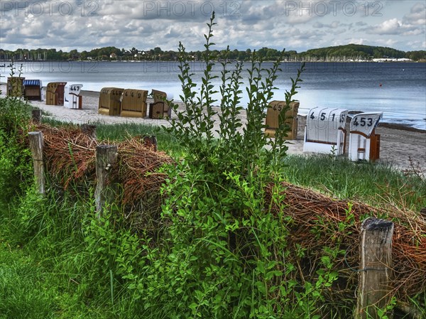 HDR image of beach chairs on the beach, grasses and wood in the foreground, cloudy sky in the