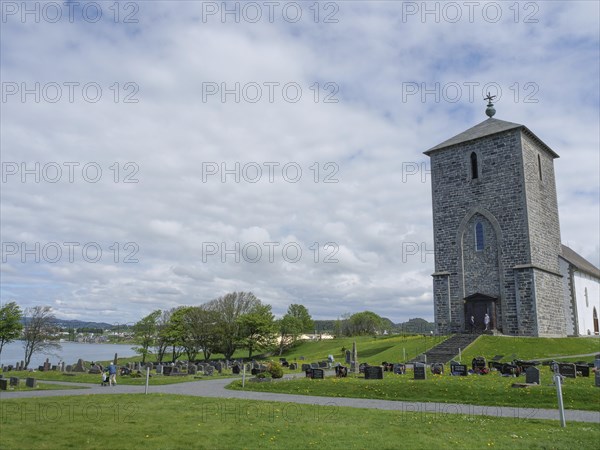 Old church on a cemetery next to a lake under a cloudy sky, old stone church and many gravestones