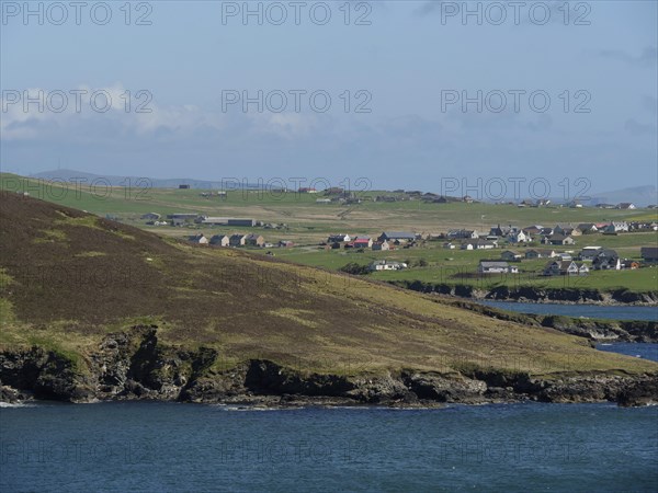 Green fields and houses on a rocky coastline overlooking the sea, green meadows on a deep blue sea
