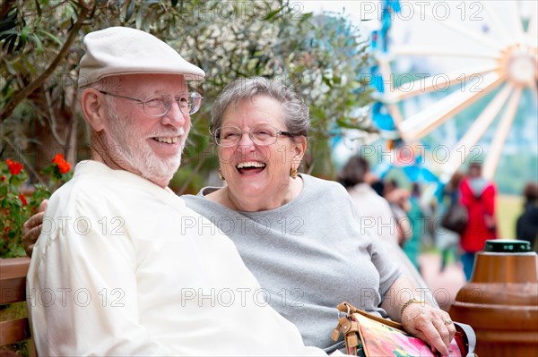 Laughing senior adult couple enjoying the carnival from the outdoor bench