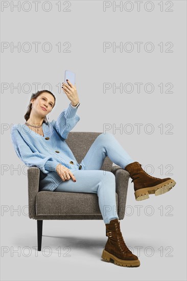 A passionate woman in a blue knitted outfit is seated comfortably on a chair, engaging with her