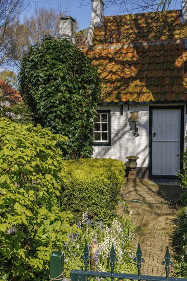 Entrance of a house surrounded by a garden with trees and hedges in spring, brick path, historic