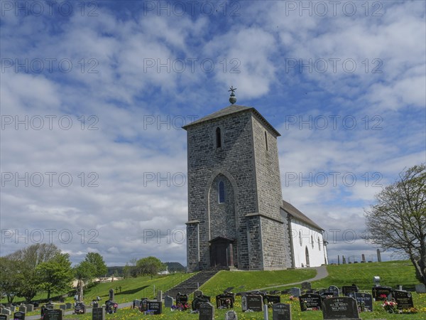 Stone church in a cemetery under a cloudy sky with trees in the background, old stone church and