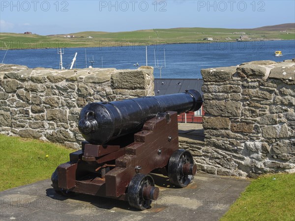 Old cannon in front of a stone wall with a view of the sea and green hills in the background, old