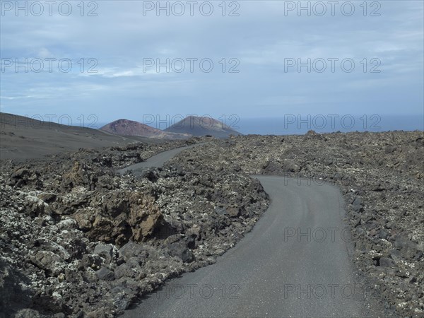A winding tarmac road through a volcanic landscape, surrounded by lava and rocks under a cloudy