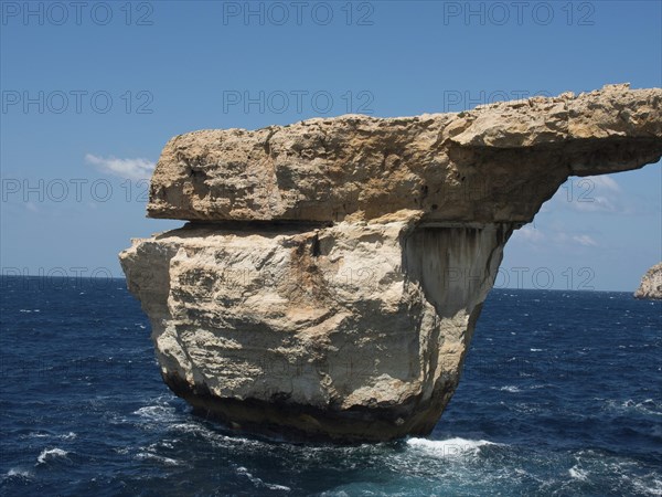 Massive rock arch towers over the sea, surrounded by cliffs under clear blue skies, many historic