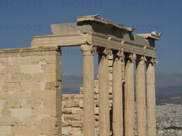 Ancient marble columns in a ruin with a part of the city in the background under a clear sky,