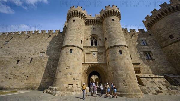 Super wide angle shot, several people admiring a mighty castle with watchtowers and blue sky in the