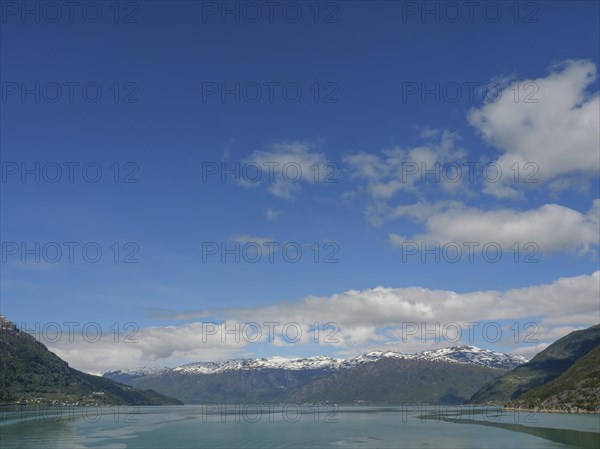 Expansive view of a mountain range under a clear blue sky with some clouds and a calm lake,