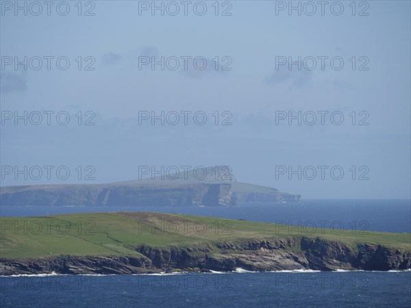 Grassy cliffs jutting into the azure sea with a distant island in the background, green meadows on