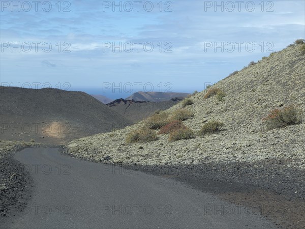 A tarmac road winds its way through overgrown, barren hills under a slightly cloudy sky, barren