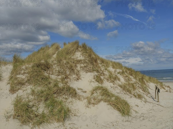 High sand dunes with grass, above a sky with some clouds, dunes on an island with a blue boat and a
