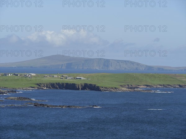 View of the tranquil coastal landscape with houses and hills in the background, green meadows by a