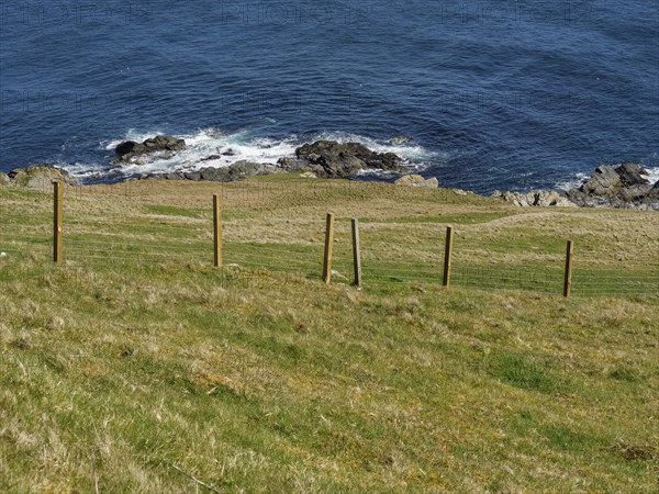 Fence along a grassy hillside overlooking the blue sea, green meadows on a deep blue sea and a