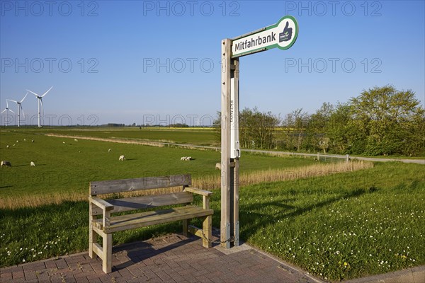 Carpooling bench in the marsh landscape with sheep and wind turbines near Simonsberg, Nordfriesland