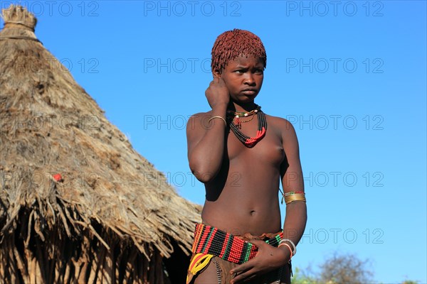 South Ethiopia, Omo region, young woman of the Hammer people standing in front of a round hut,
