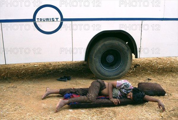 Attendant sleeping near the bus where he is employed, teenage boy working in poor conditions work,