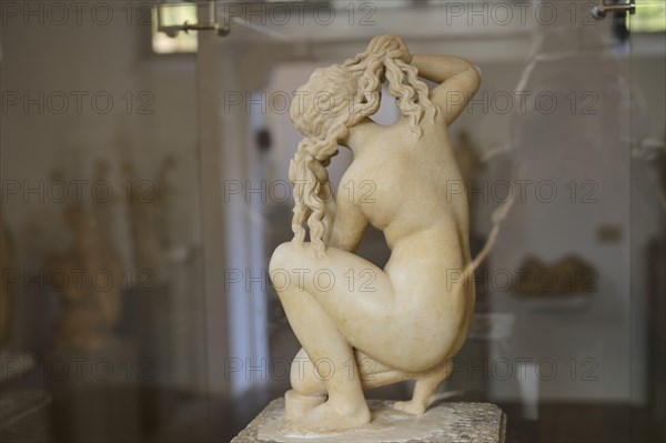 Aphrodite, crouching, rear view, sculpture of a naked woman tying her hair in a classical style in