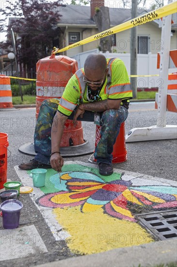 Detroit, Michigan, Artist Trae Isaac paints a design on a city street. He is part of City Walls, a