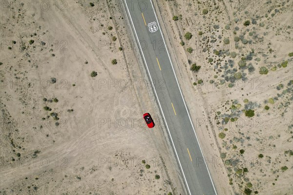 Drone shot of Route 66 with Route 66 sign on the road and red Ford Mustang convertible, Mojave