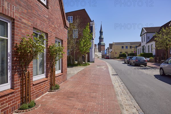 Street, house with rose bushes, buildings and St Laurentius Church in Toenning, Nordfriesland