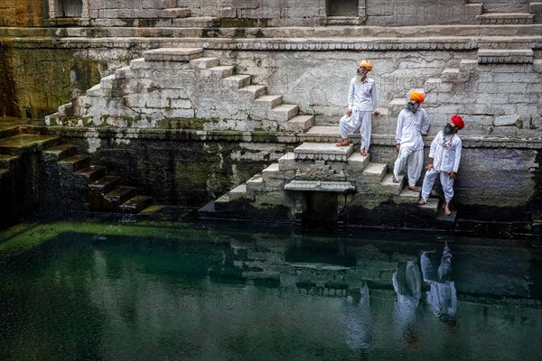 Three traditional men with turban at the steps at the stepwell Toorji Ka Jhalra in Jodhpur,