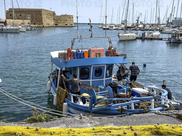In the foreground yellow fishing net from behind local Greek fishermen arranging their nets on