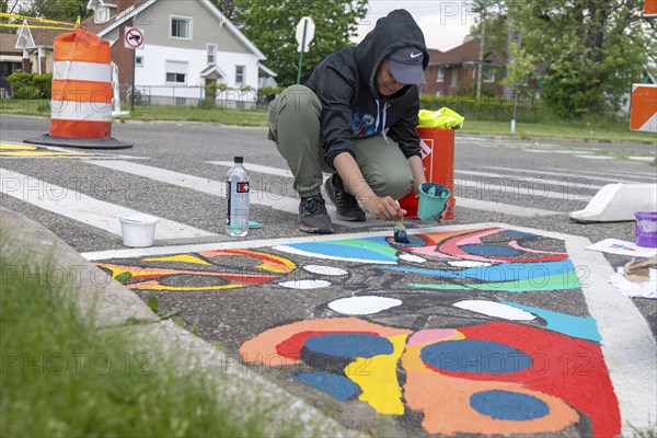 Detroit, Michigan, Artist Simone Lancaster paints a design on a city street. She is part of City
