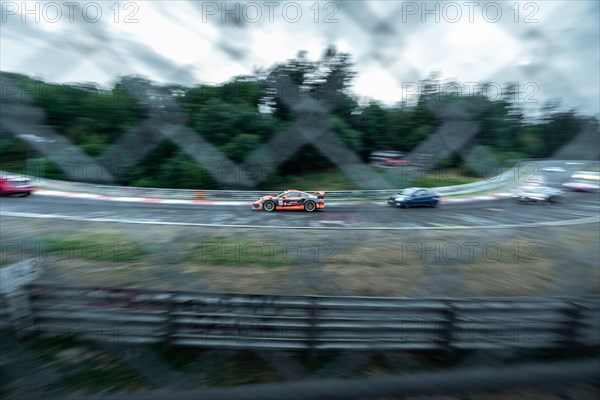 A racing car in action, captured with motion blur and visible through a fence. Nuerburgring race
