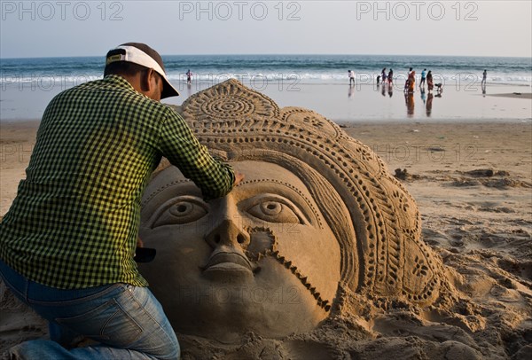 Sand artist sculpting a sand sculpture, sculpture representing the hindu goddess Lakshmi, beach at