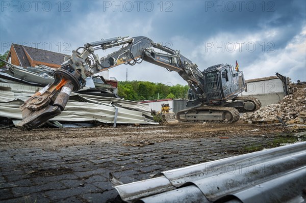 A heavy excavator lifts materials on a construction site full of rubble and pieces of metal, grey