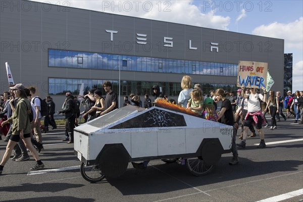 Participants with a Cybertruck cardboard model on a bicycle and sign Hands off our water in front