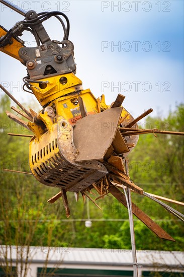 Large yellow hydraulic grab on an excavator lifting pieces of wood, with green background,