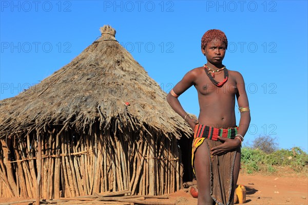 South Ethiopia, Omo region, young woman of the Hammer people standing in front of a round hut,